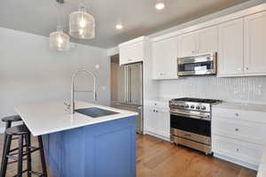 Kitchen featuring pendant lighting, a center island with sink, sink, tasteful backsplash, and premium appliances