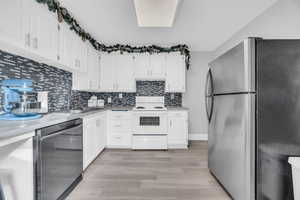 Kitchen with sink, stainless steel appliances, tasteful backsplash, white cabinets, and light wood-type flooring