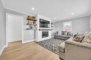 Living room with hardwood / wood-style floors, crown molding, and a fireplace