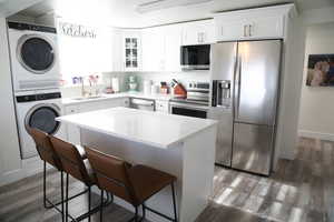 Kitchen featuring stacked washing maching and dryer, stainless steel appliances, sink, white cabinets, and a kitchen island