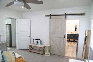 Interior space featuring wooden walls, ensuite bath, ceiling fan, a barn door, and stainless steel refrigerator