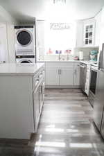 Kitchen featuring stacked washing maching and dryer, light wood-type flooring, stainless steel appliances, and white cabinetry