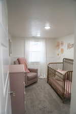 Bedroom with a crib, a textured ceiling, and dark colored carpet