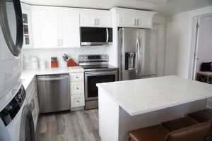 Kitchen featuring a breakfast bar, stacked washer and dryer, stainless steel appliances, and white cabinetry