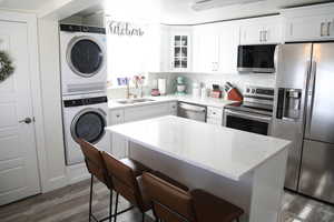 Kitchen with sink, stainless steel appliances, light stone counters, white cabinets, and stacked washer and clothes dryer