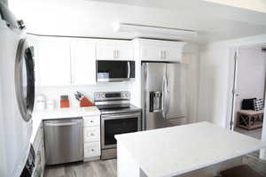 Kitchen featuring backsplash, light hardwood / wood-style flooring, appliances with stainless steel finishes, light stone counters, and white cabinetry