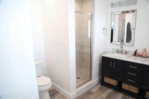 Bathroom with hardwood / wood-style floors, vanity, toilet, and an enclosed shower