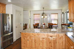 Kitchen with hanging light fixtures, an inviting chandelier, stainless steel fridge with ice dispenser, light stone counters, and dark hardwood / wood-style floors