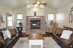 Living room featuring hardwood / wood-style floors, ceiling fan, a stone fireplace, and vaulted ceiling