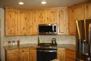 Kitchen with light stone countertops, stainless steel appliances, and tasteful backsplash