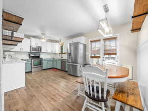 Kitchen with white cabinets, backsplash, stainless steel appliances, and hanging light fixtures