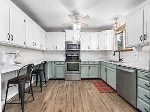 Kitchen featuring pendant lighting, sink, green cabinetry, light wood-type flooring, and stainless steel appliances