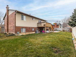 Back of house with cooling unit, a yard, a patio, and a wooden deck