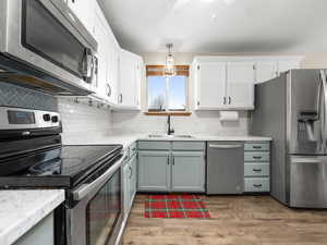 Kitchen featuring backsplash, stainless steel appliances, sink, white cabinetry, and hanging light fixtures