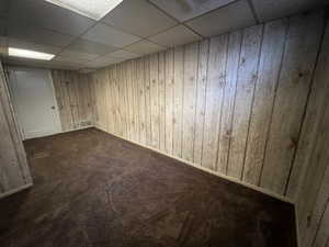 Basement featuring wood walls, a drop ceiling, and dark carpet