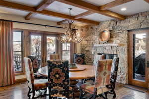 Dining area with a stone fireplace, hardwood / wood-style floors, french doors, and a notable chandelier