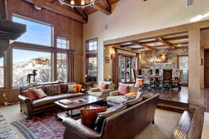 Living room with wooden walls, beam ceiling, a chandelier, a high ceiling, and carpet floors