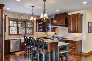 Kitchen with dark wood-type flooring, a kitchen island, custom range hood, stainless steel appliances, and a chandelier