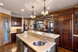 Kitchen with sink, dark wood-type flooring, an island with sink, a chandelier, and decorative light fixtures