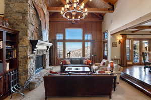 Carpeted living room with high vaulted ceiling, an inviting chandelier, a fireplace, beamed ceiling, and wood ceiling