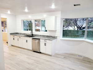 Kitchen with light stone counters, dishwasher, and white cabinets