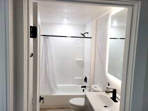 Full bathroom with shower / bath combination with curtain, toilet, a textured ceiling, and vanity