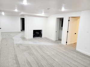 Basement featuring light colored carpet, a textured ceiling, and a brick fireplace