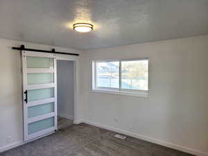 Unfurnished bedroom with carpet, a barn door, and a textured ceiling