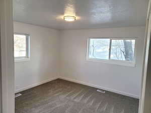 Unfurnished room with a textured ceiling and dark carpet