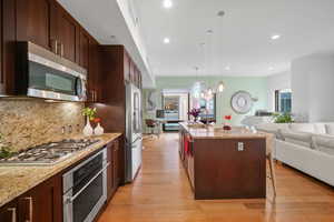 Kitchen featuring light stone countertops, a kitchen island with sink, pendant lighting, and stainless steel appliances