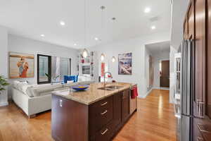 Kitchen featuring light stone countertops, sink, hanging light fixtures, a kitchen island with sink, and dark brown cabinets