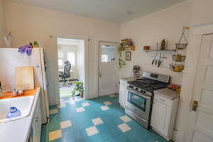 Kitchen featuring white cabinets, stainless steel gas stove, white fridge, and sink