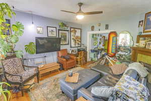 Living room with ceiling fan, a fireplace, light wood-type flooring, and a textured ceiling