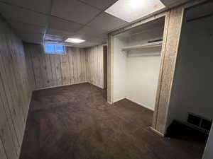 Basement with wood walls, a drop ceiling, and dark carpet