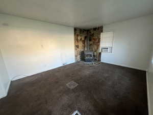 Unfurnished living room featuring dark carpet, a wood stove, and cooling unit