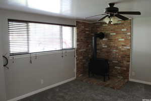 Unfurnished living room with dark carpet, a wood stove, a wealth of natural light, and ceiling fan