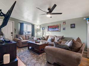 Living room with ceiling fan, wood-type flooring, and a textured ceiling