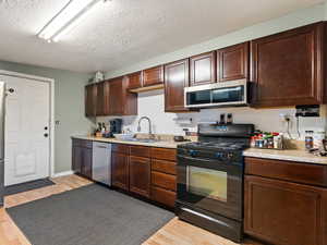 Kitchen with a textured ceiling, stainless steel appliances, light hardwood / wood-style flooring, and sink