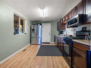 Kitchen with light stone counters, a textured ceiling, stainless steel appliances, sink, and light hardwood / wood-style floors