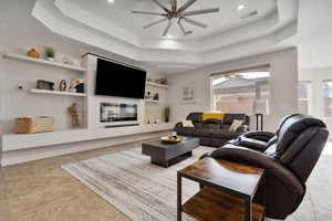 Living room with a raised ceiling, built in shelves, and ceiling fan