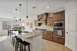 Kitchen with light stone countertops, appliances with stainless steel finishes, a breakfast bar, a kitchen island with sink, and hanging light fixtures