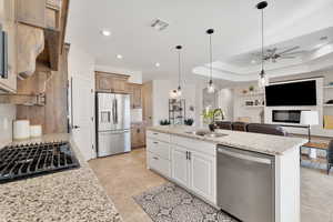 Kitchen featuring sink, ceiling fan, appliances with stainless steel finishes, a tray ceiling, and white cabinetry