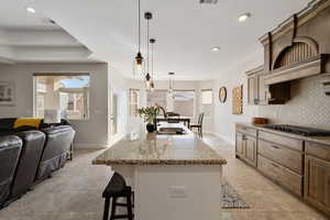 Kitchen featuring sink, a healthy amount of sunlight, an island with sink, pendant lighting, and decorative backsplash