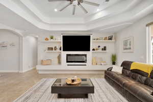 Living room featuring built in shelves, a tray ceiling, and ceiling fan