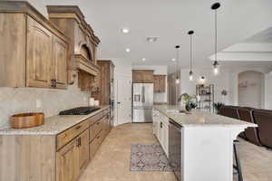 Kitchen with sink, light stone countertops, tasteful backsplash, decorative light fixtures, and stainless steel appliances