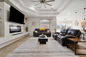 Tiled living room featuring a raised ceiling, built in shelves, ceiling fan, and sink