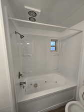 Bathroom with washtub / shower combination, hardwood / wood-style floors, a textured ceiling, and toilet