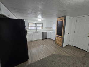 Kitchen featuring dishwasher, white cabinets, black refrigerator, sink, and light wood-type flooring