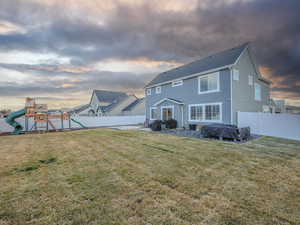 Back house at dusk with a playground and a lawn