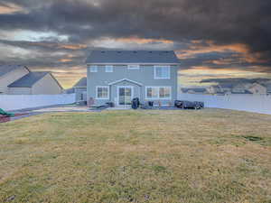 Back house at dusk featuring a patio area and a yard